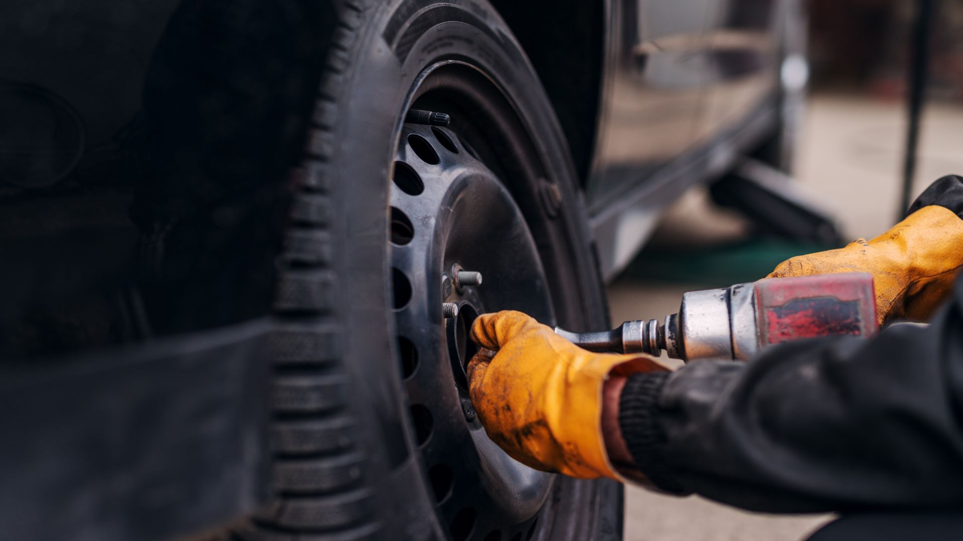 Mechanic using power drill to change tire with yellow work gloves