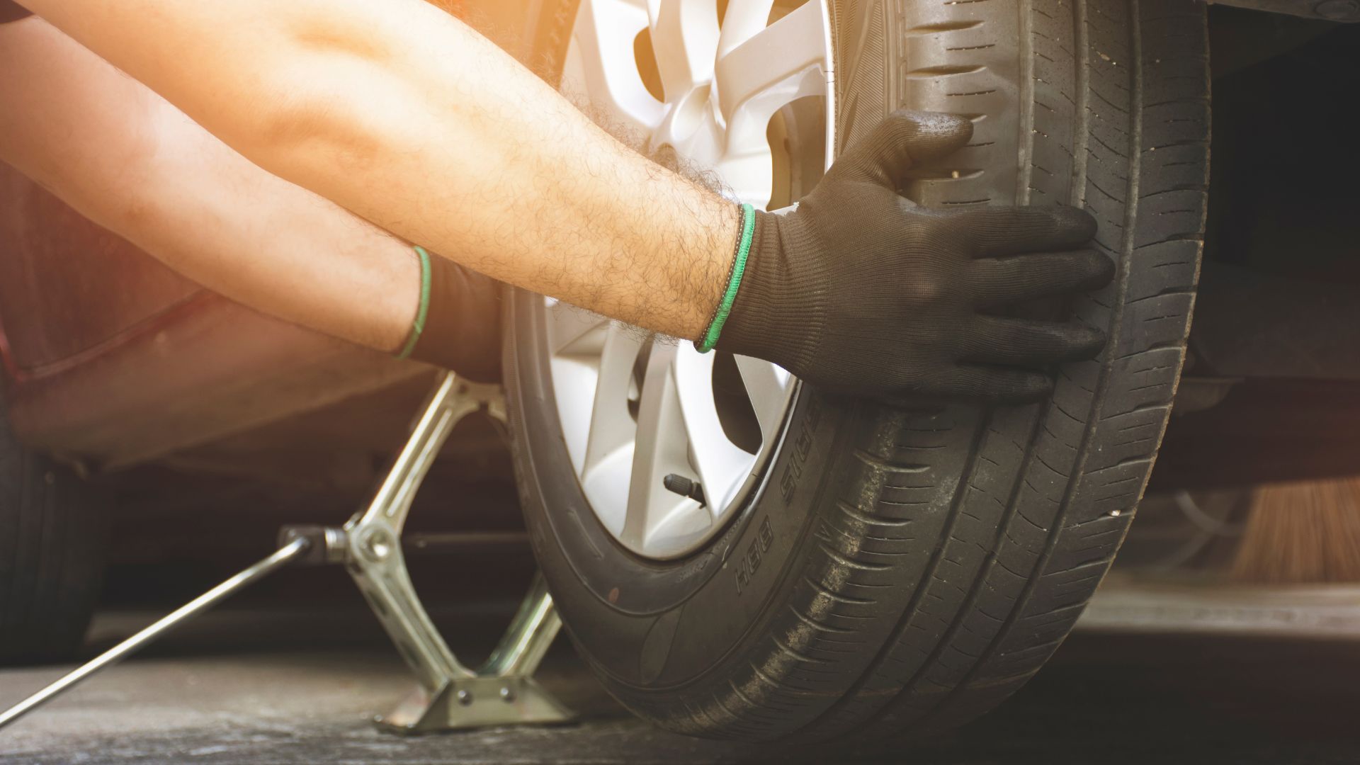 Hands changing a car tire with jack and black gloves