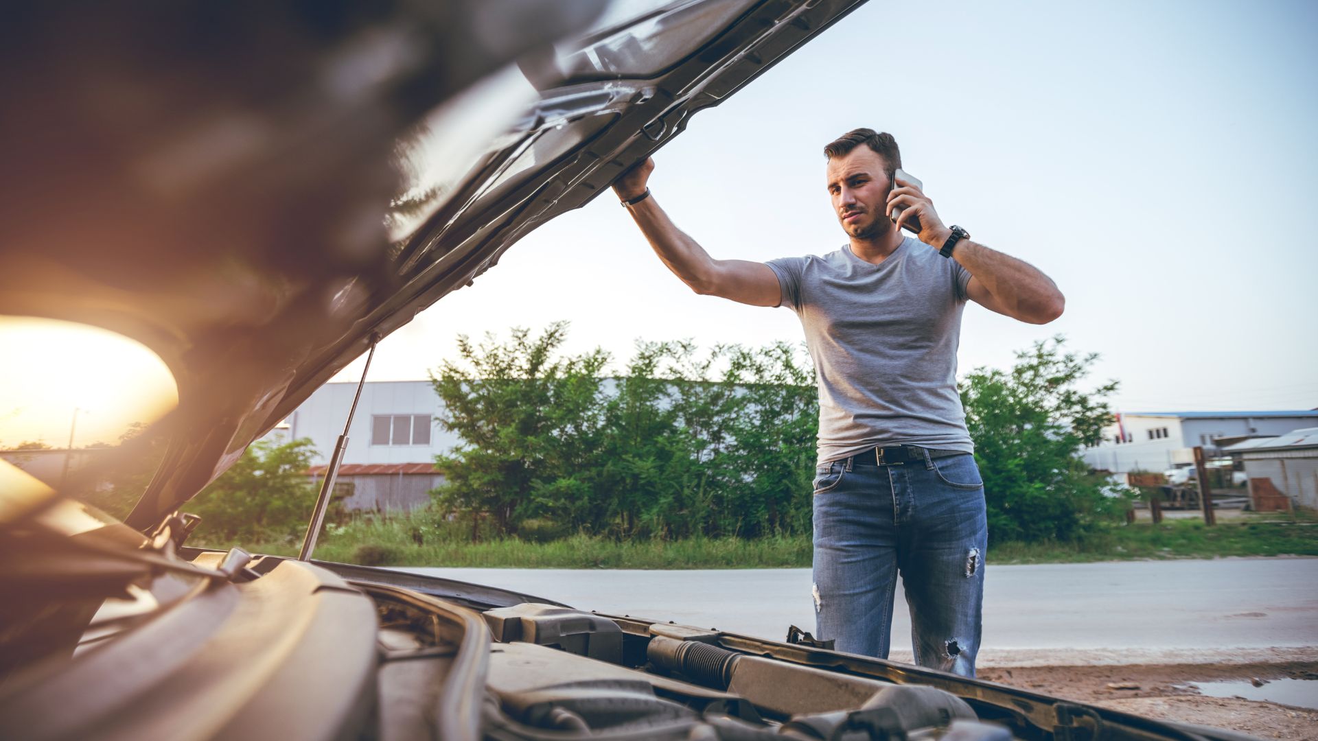 Man with open car hood talking on phone, possibly experiencing car trouble