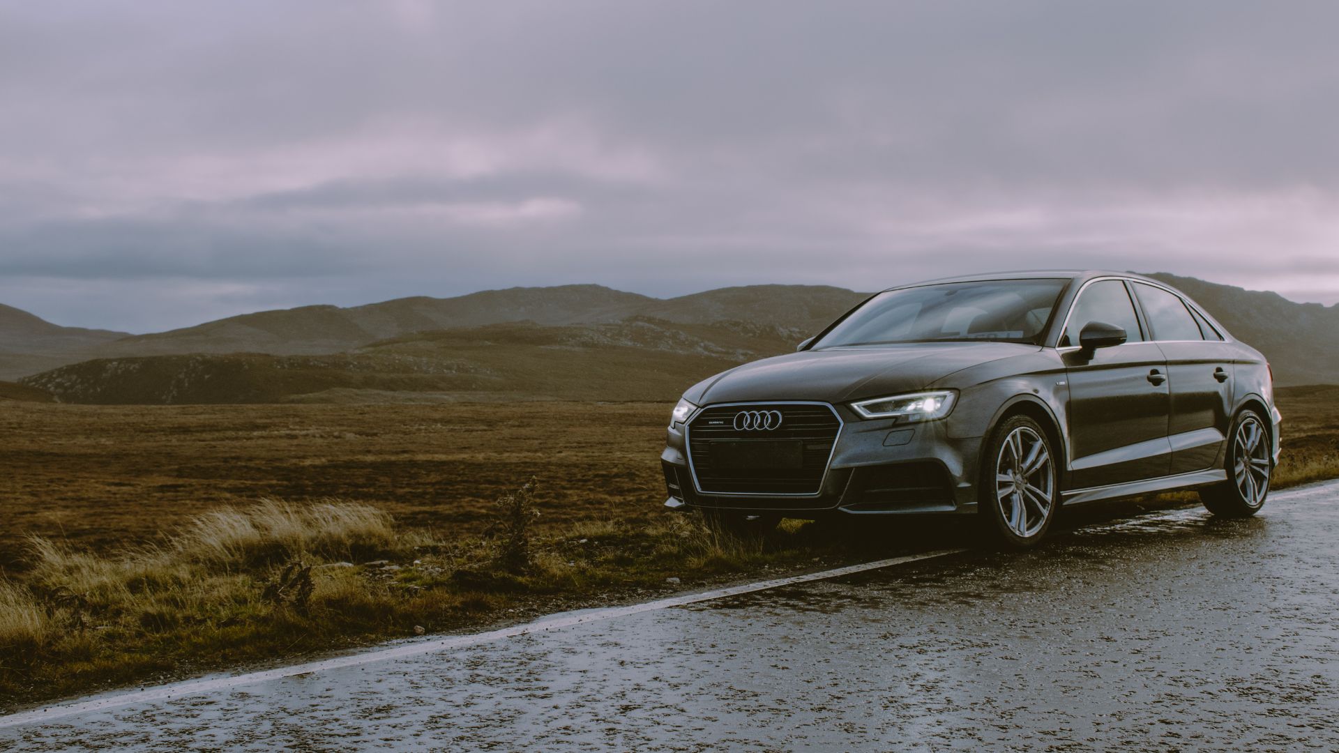 Black Audi sedan parked on wet road with misty mountain landscape