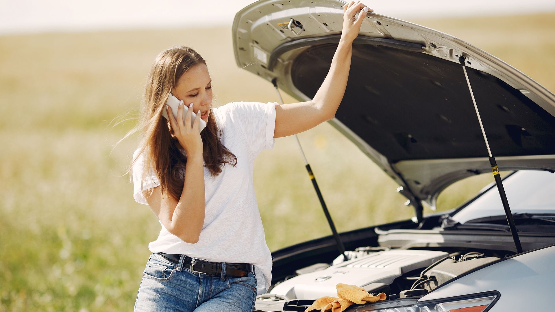 Woman calling for help with broken down car in rural field